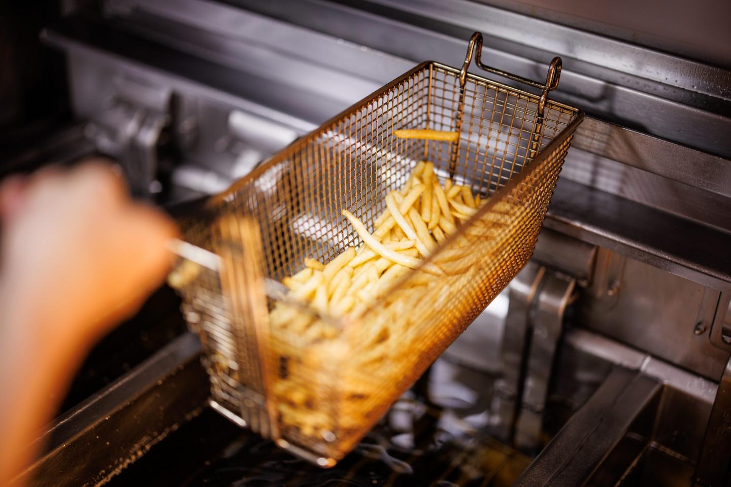 An employee takes a basket of French fries out of the fryer at a branch of the McDonald's fast food chain on Martin-Luther-Strasse in Giesing.