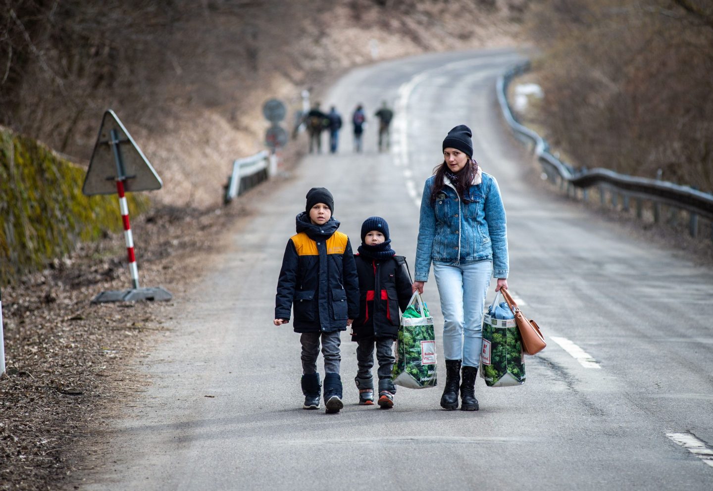 A woman with two children and carrying bags walk on a street to leave Ukraine after crossing the Slovak-Ukrainian border in Ubla, eastern Slovakia, close to the Ukrainian city of Welykyj Beresnyj, on February 25, 2022, following Russia's invasion of the Ukraine.
