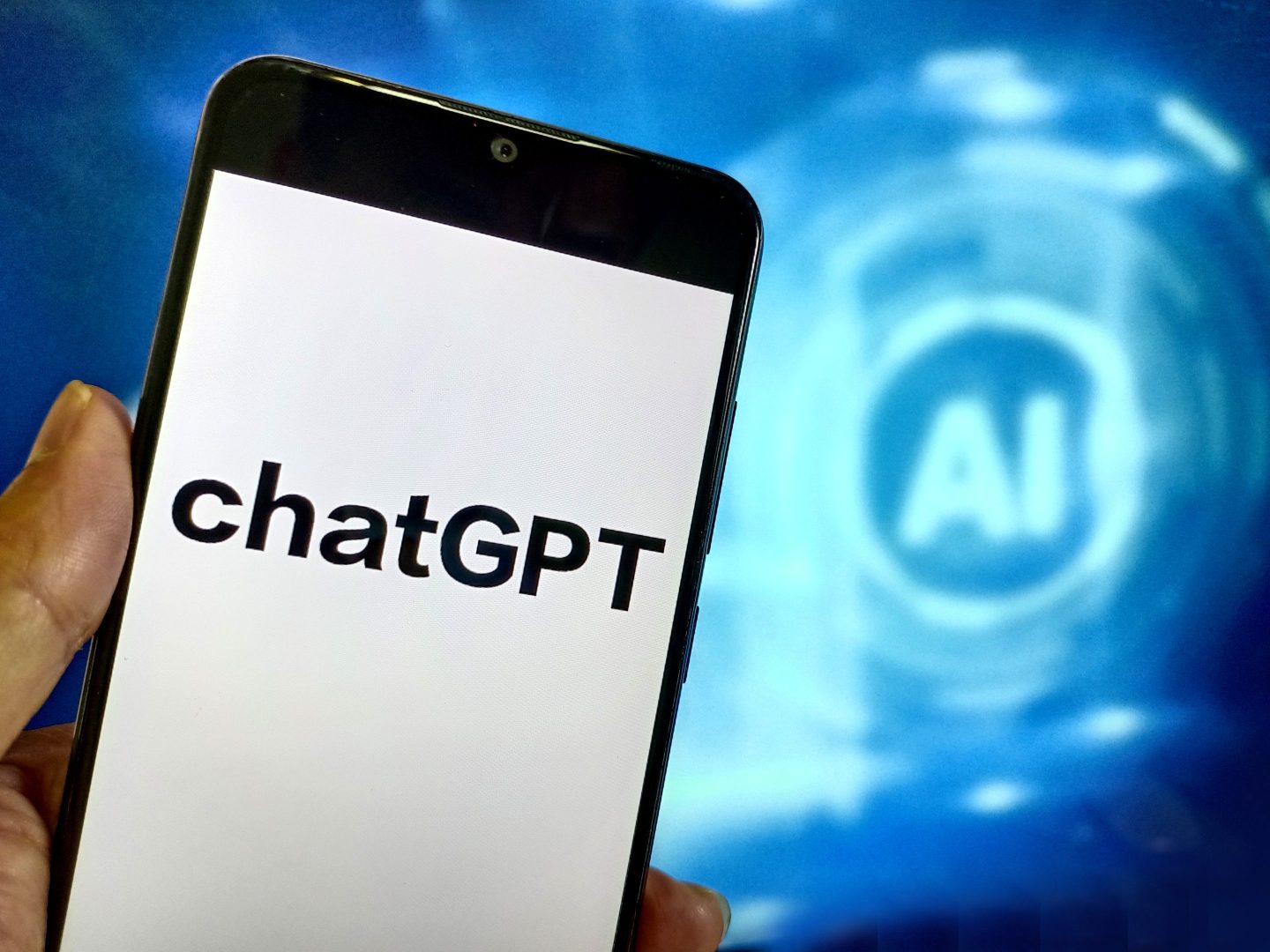 Phone with ChatGPT on the screen in front of a larger screen with AI written on it