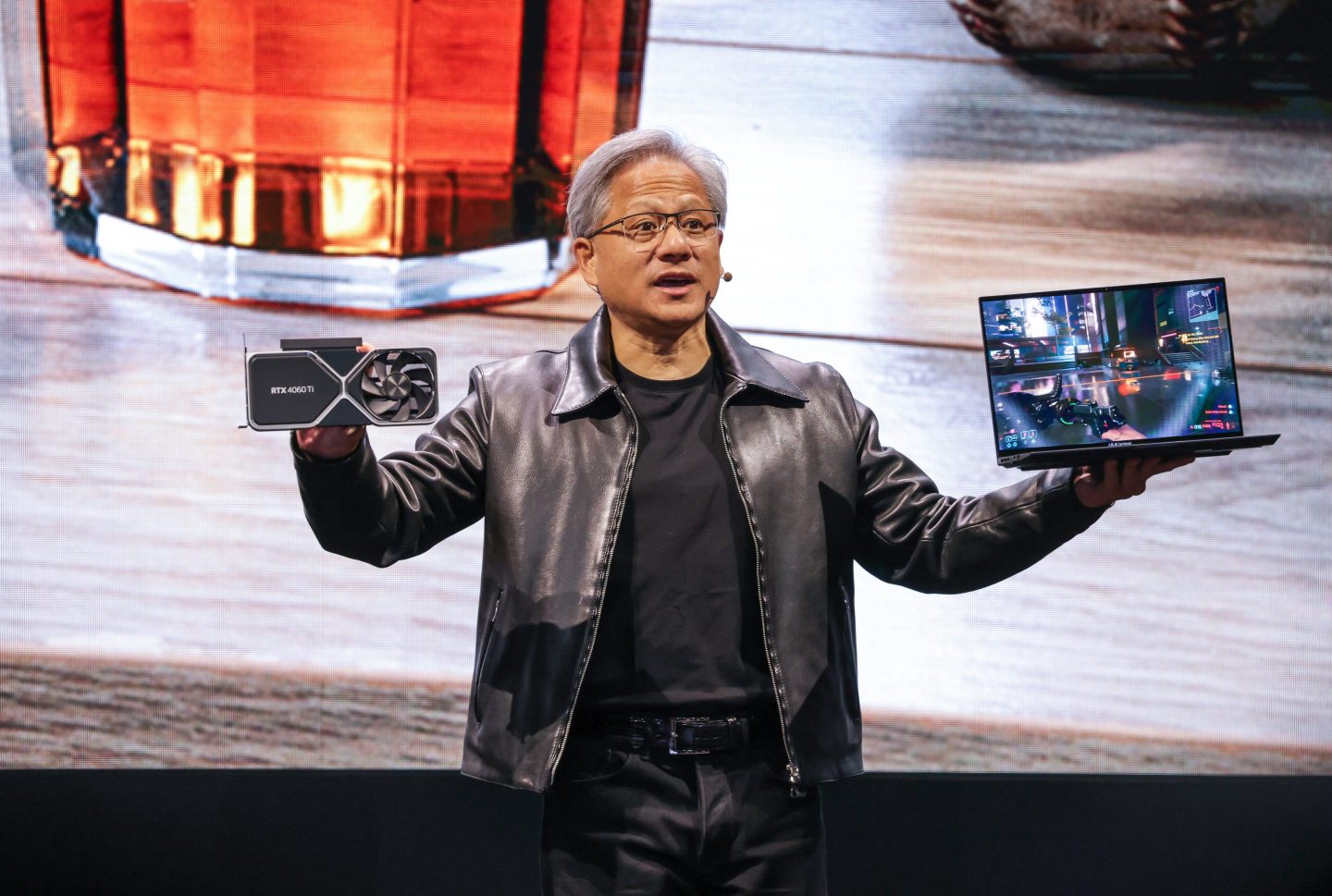 A picture of Jensen Huang holding a laptop on one hand and a new device on the other hand