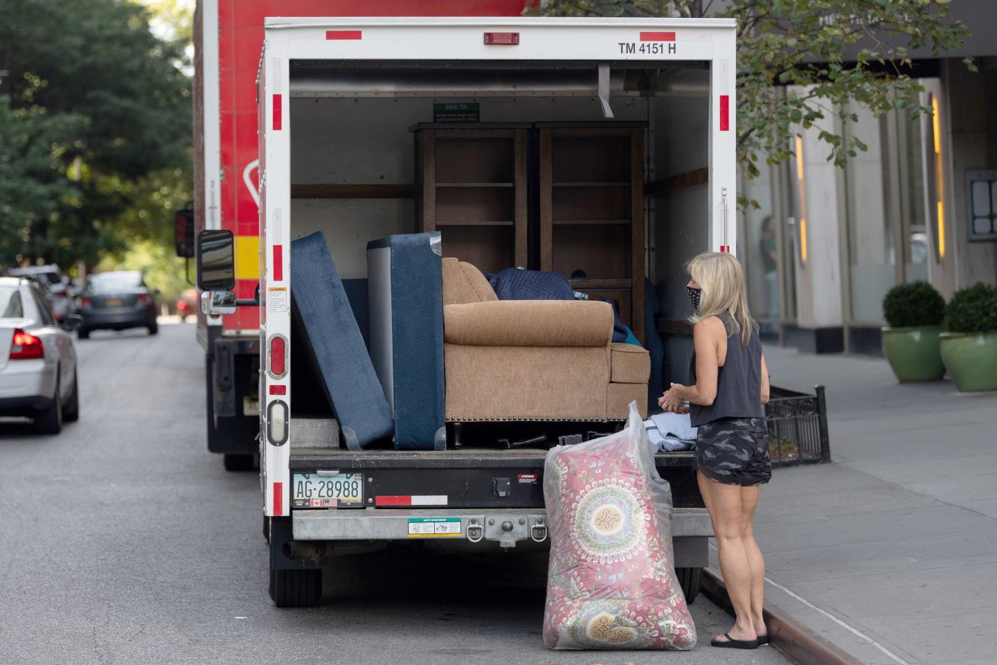 A woman wearing a mask loads items into a Uhaul moving truck.