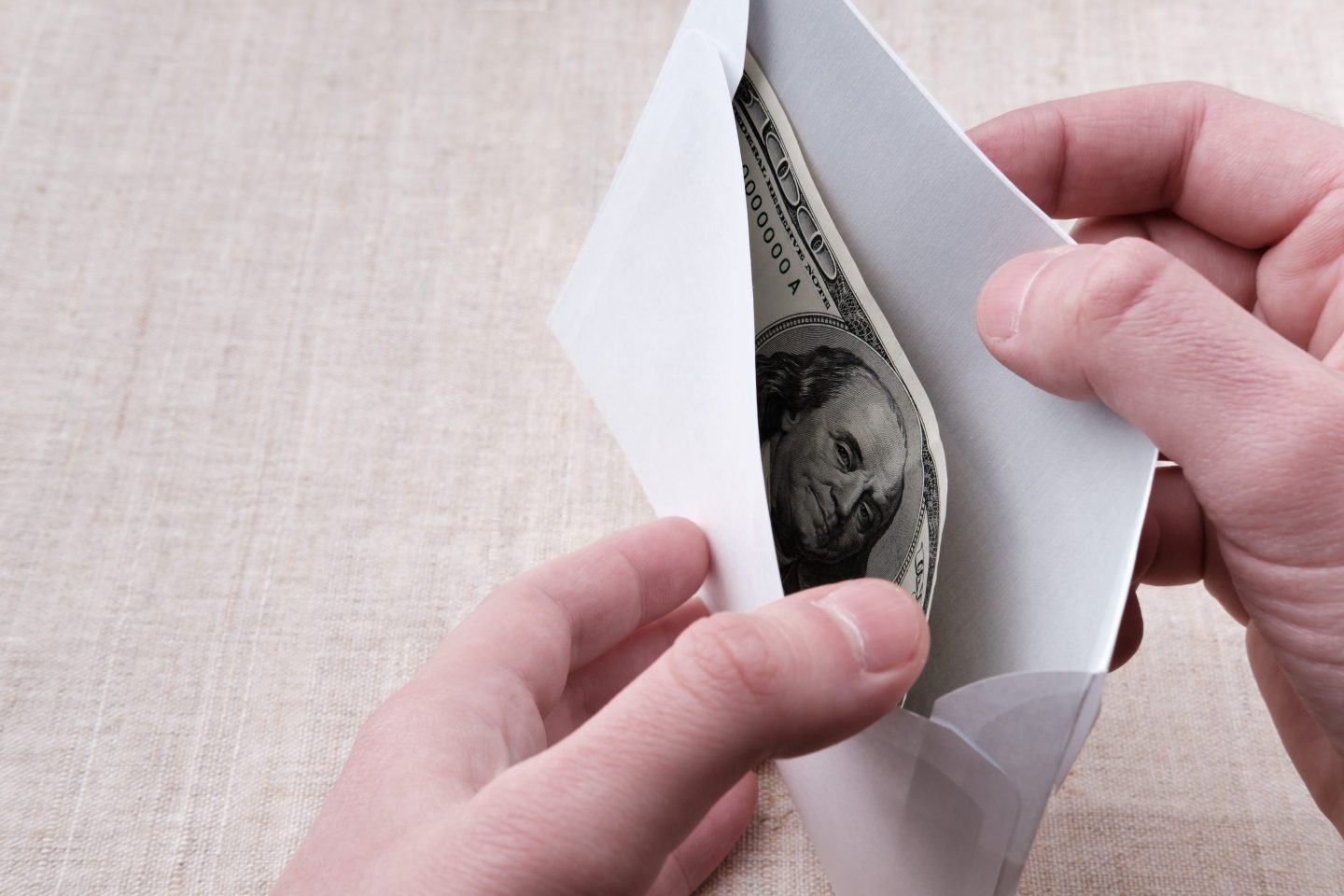 hands open an envelope to reveal a $100 bill.