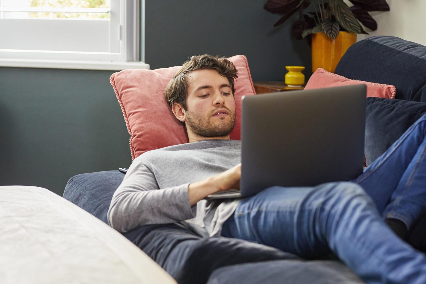 man lying on couch with laptop