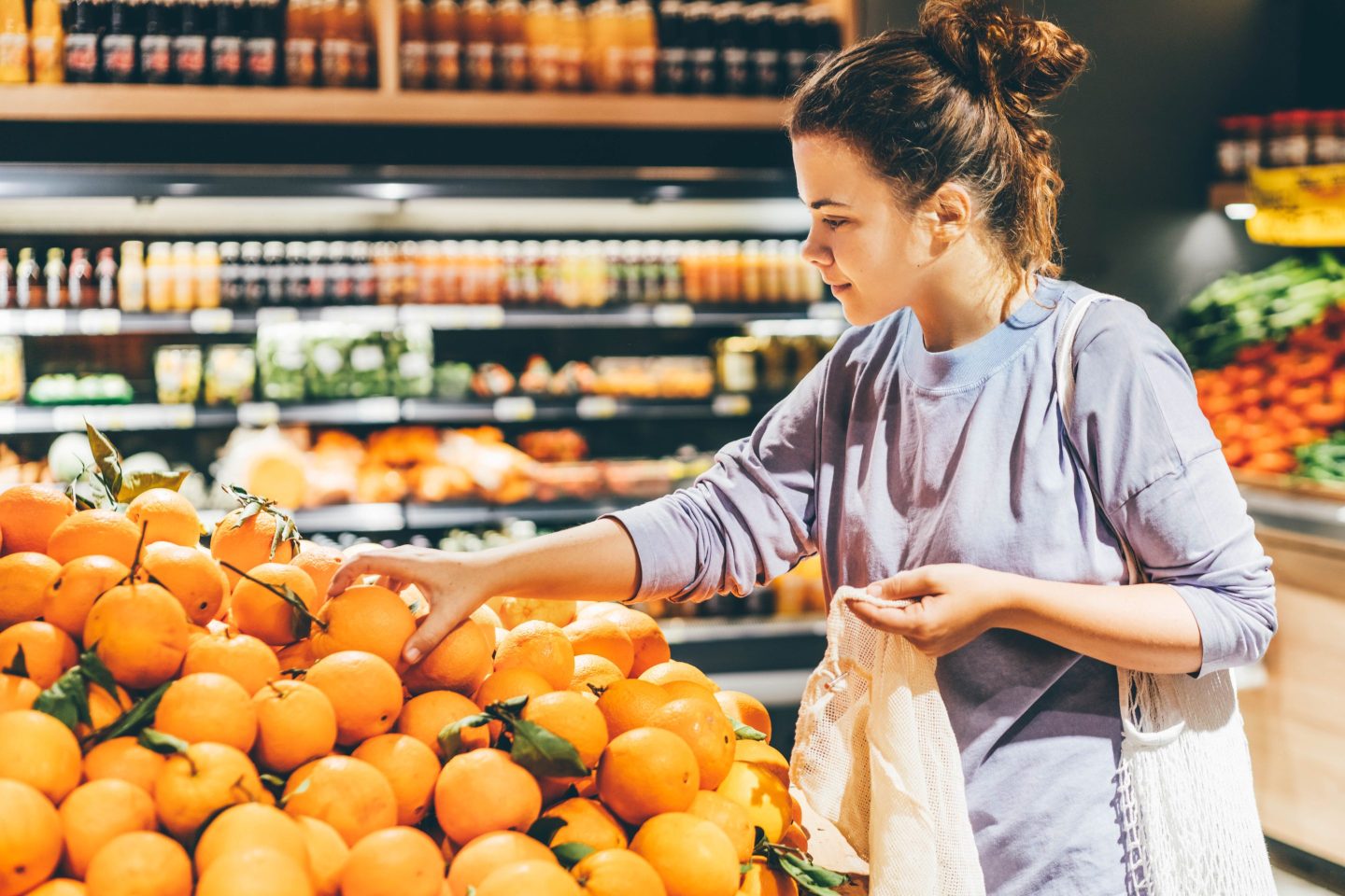 Woman choosing orange at market and using reusable eco bag.