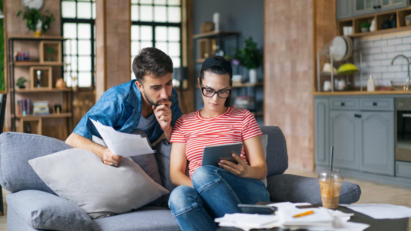 Couple calculating bills at home using tablet and calculator.