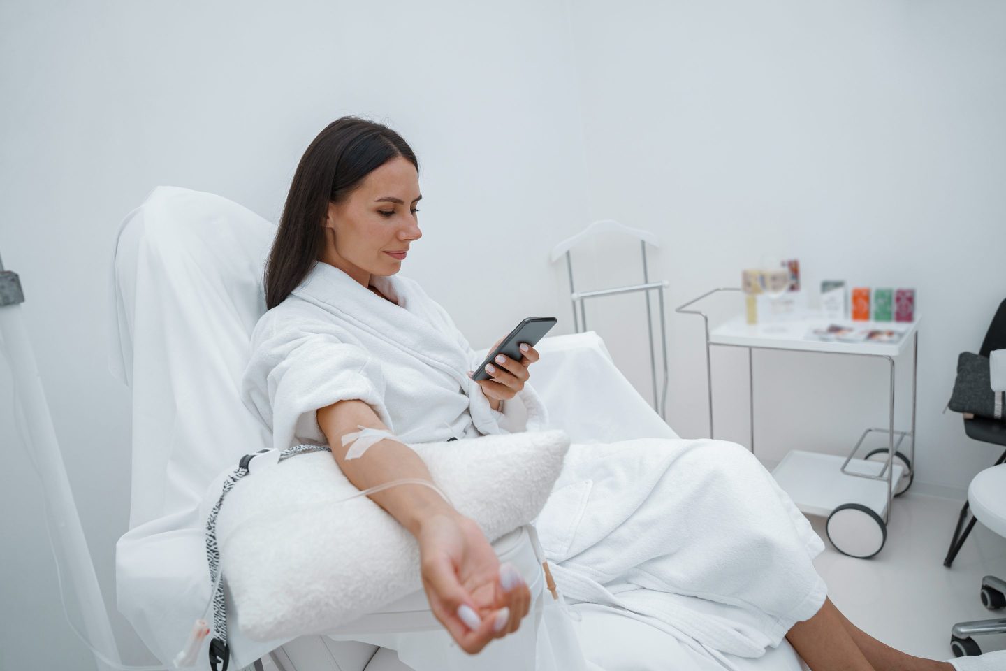 Woman in white bathrobe use phone during medical procedure in beauty clinic