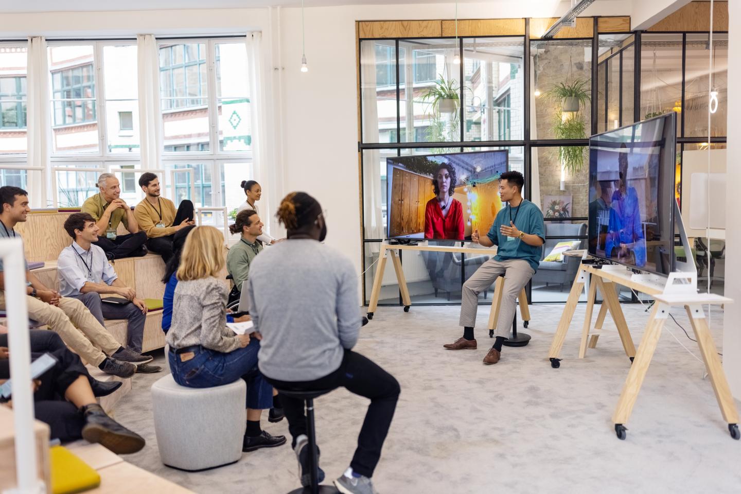 Asian man addressing businesspeople during meeting with two colleagues attending via video call seen on television screen. Business people having hybrid meeting in office.