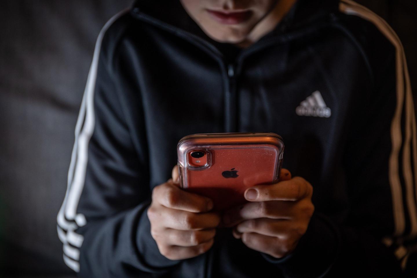 A 12-year-old boy looks at a smartphone screen