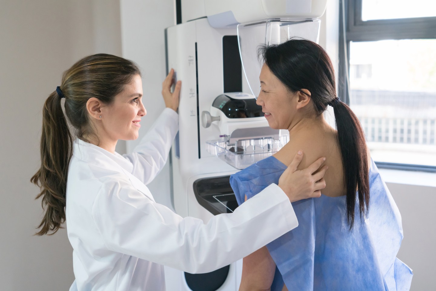 Female gynecologist helping a patient get in position for a mammogram.