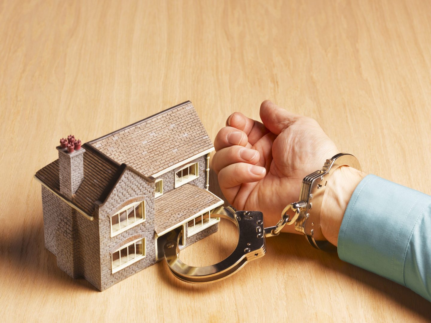 Photo of a person handcuffed to a small model of a house