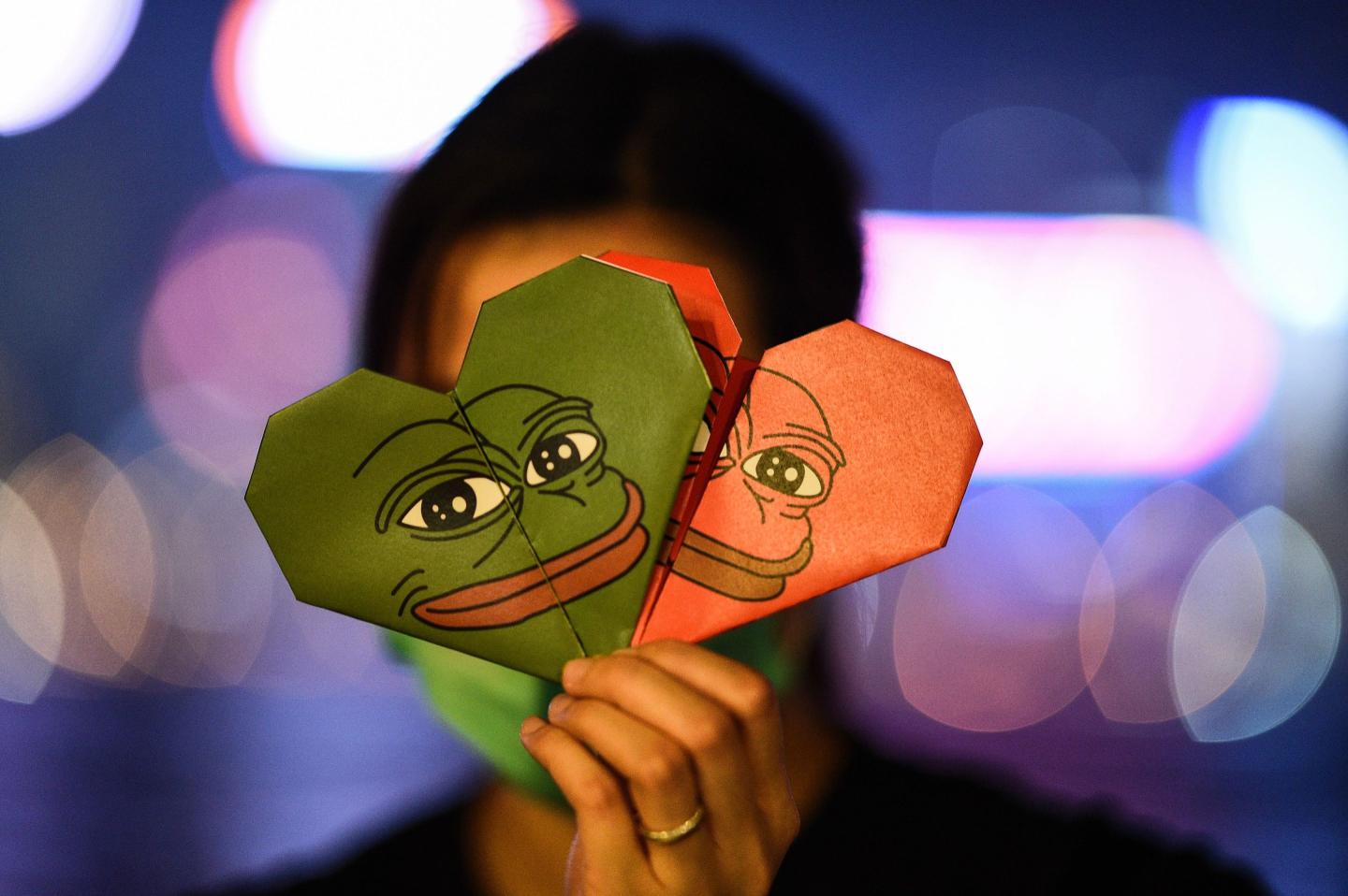 A protester in Hong Kong holds origami hearts with a depiction of Pepe.