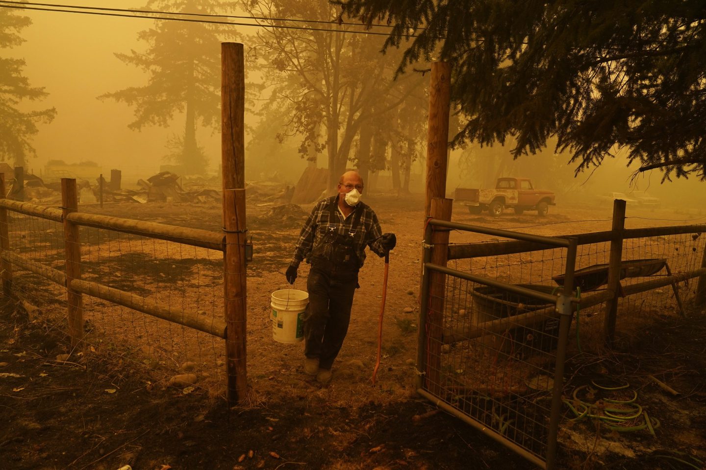 George Coble carries a bucket of water to put out a tree still smoldering on his property destroyed by a wildfire on Sept. 12, 2020, in Mill City, Ore.