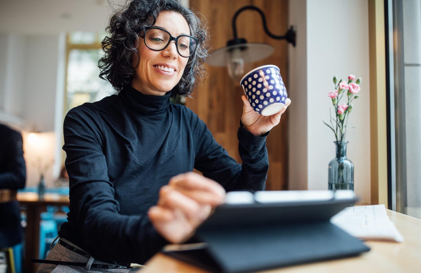 A woman on using a tablet while holding a mug.