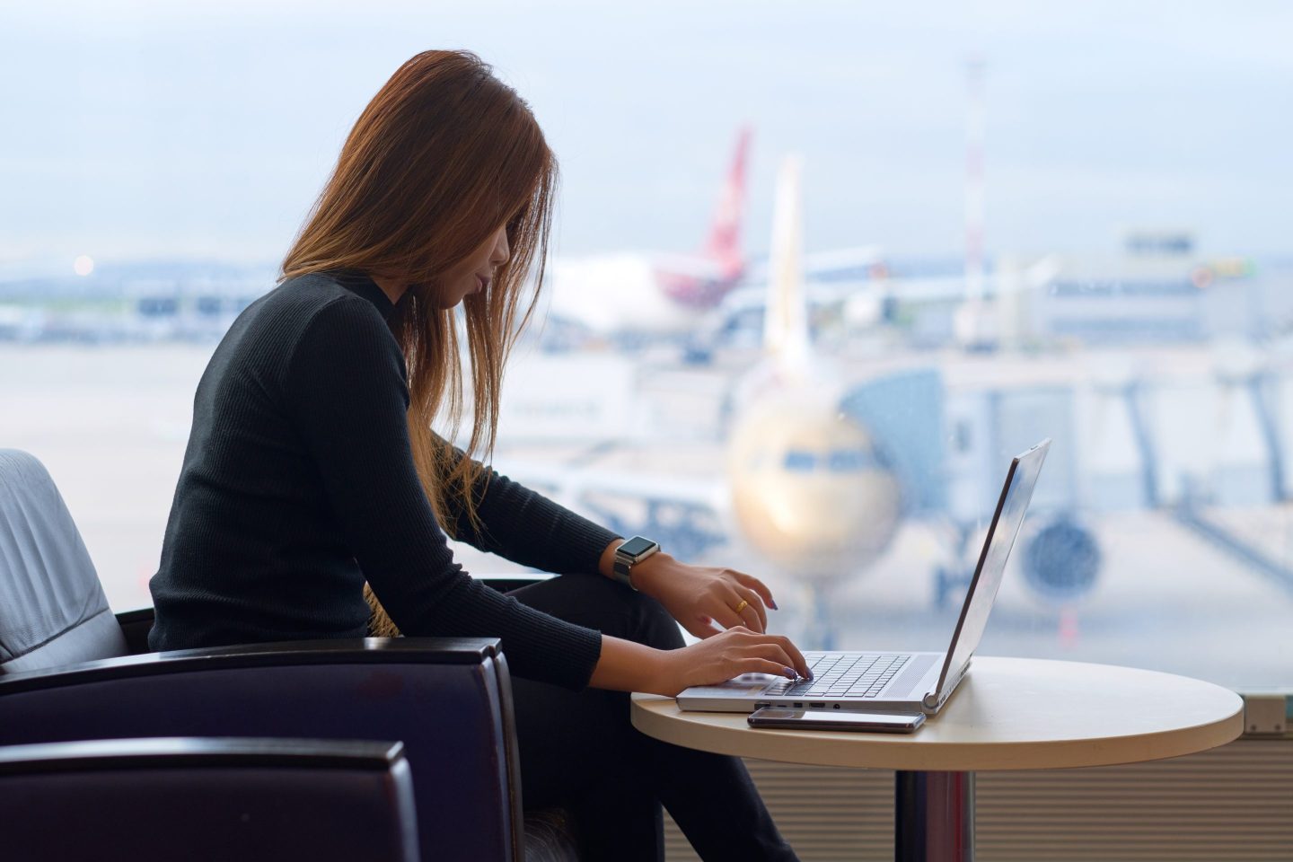 Woman working on laptop in airport.
