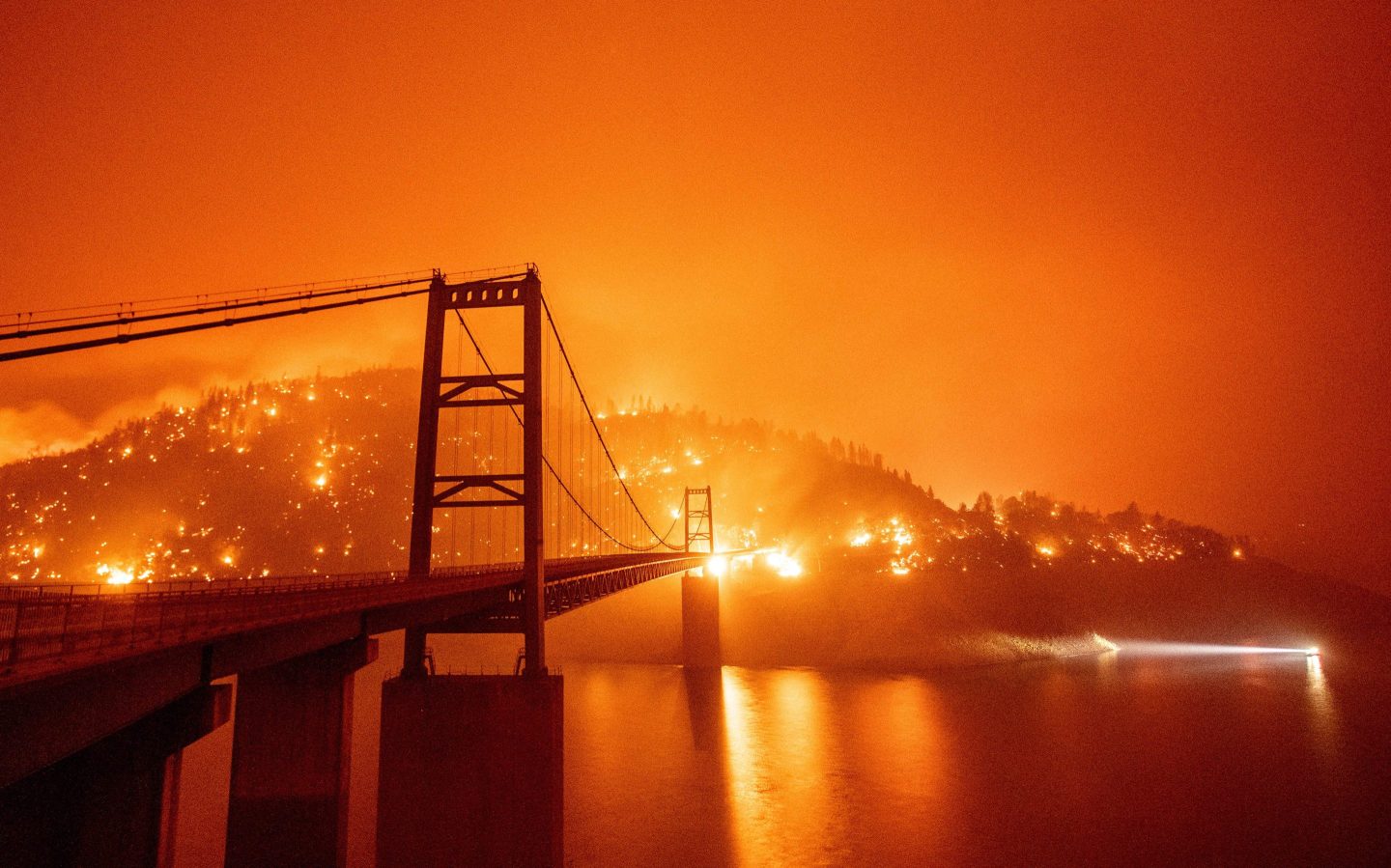 A boat motors by as the Bidwell Bar Bridge is surrounded by fire in Lake Oroville during the Bear fire in Oroville, California