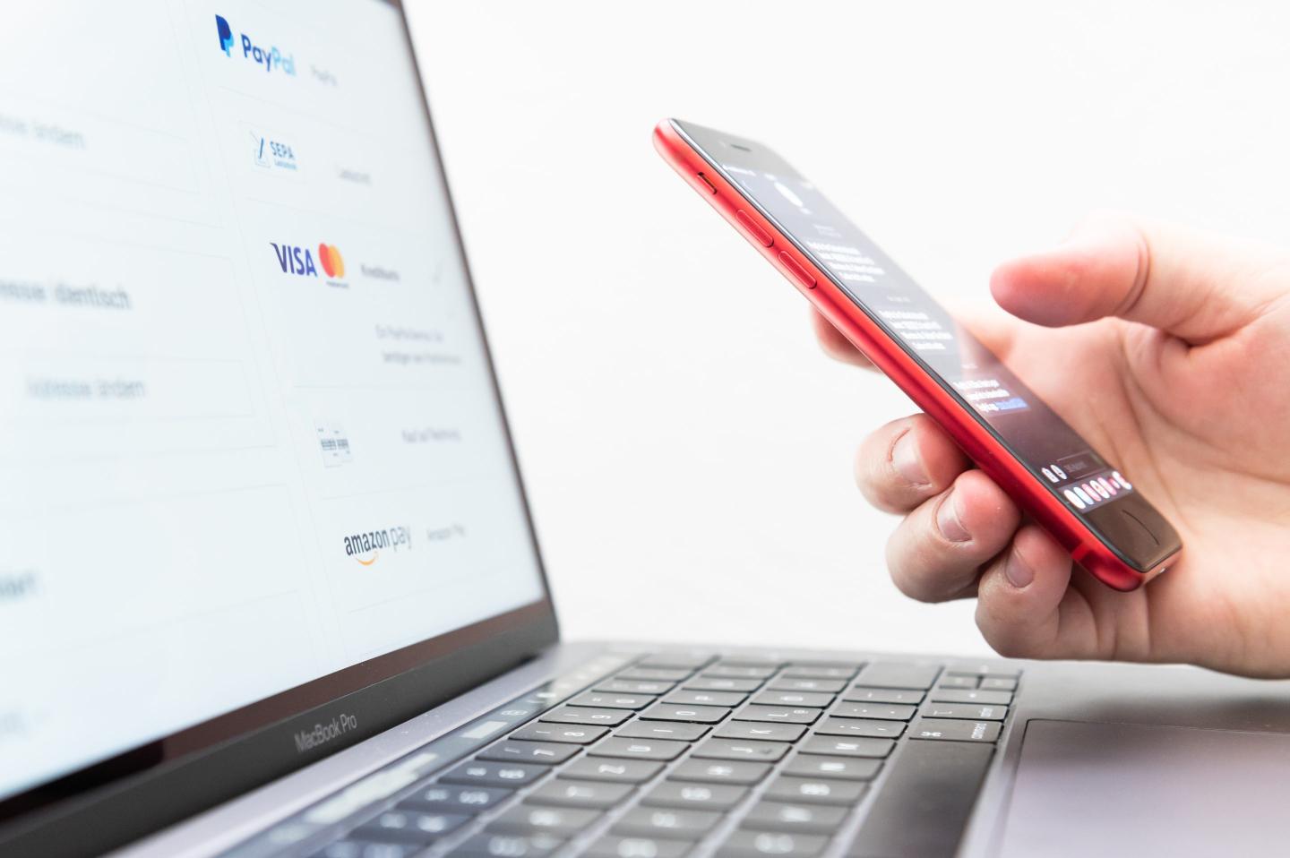 A person holding an iPhone next to a laptop