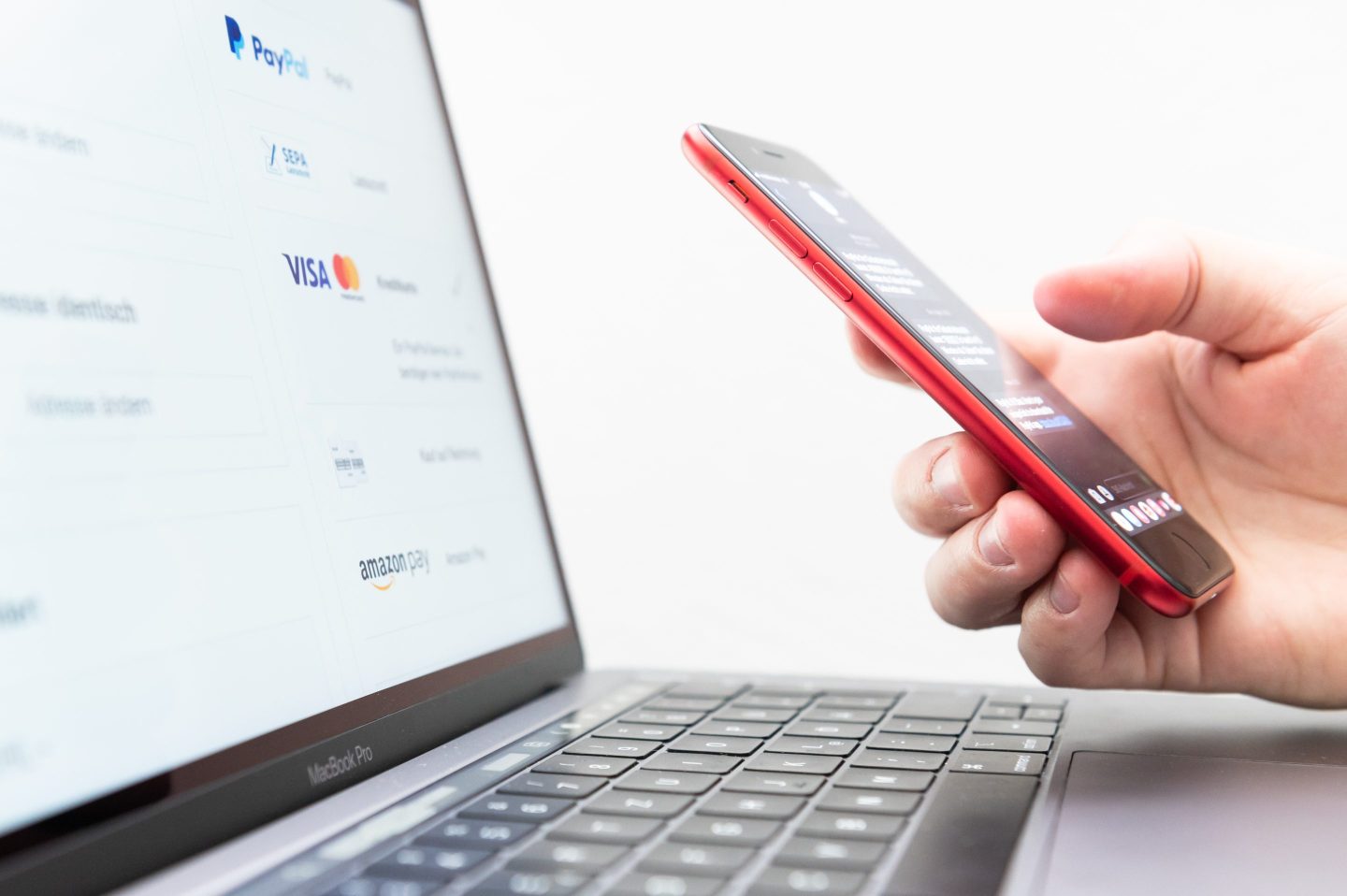 A person holding an iPhone next to a laptop