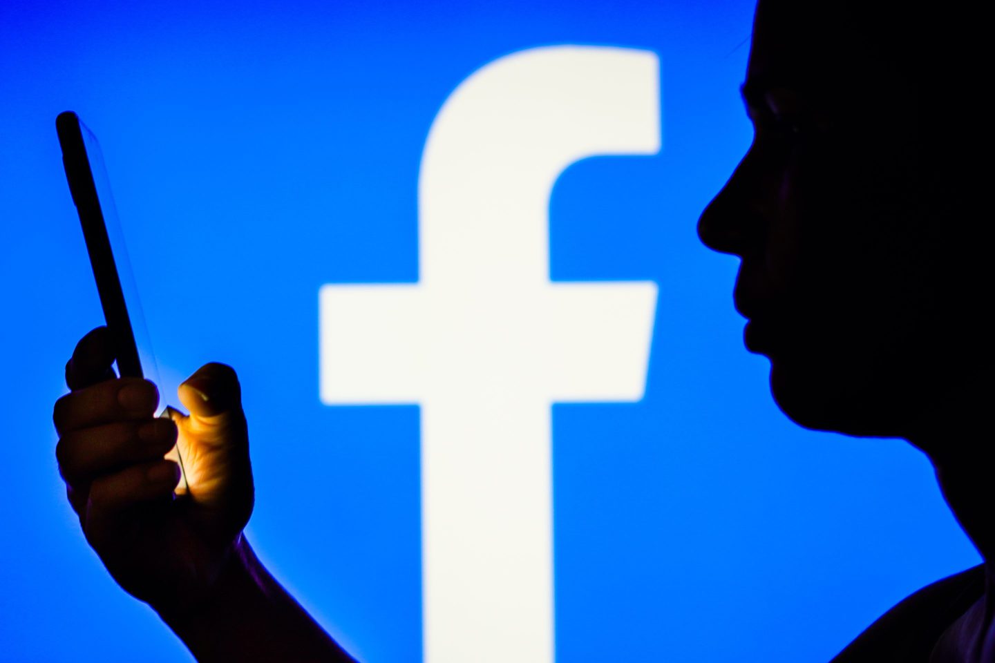 a woman's silhouette holds a smartphone with the Facebook logo in the background.