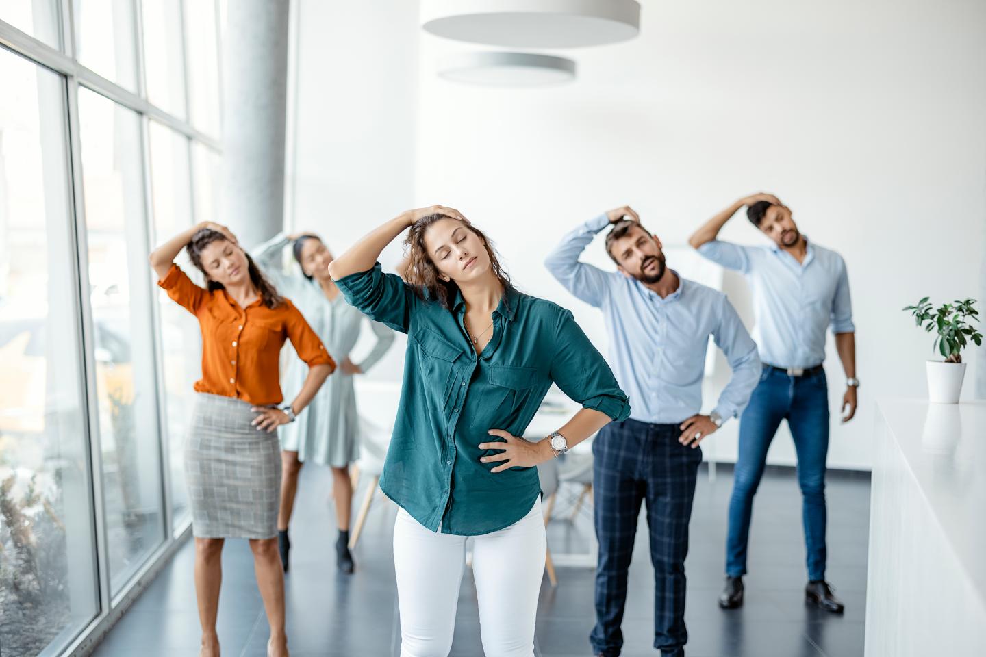 Photo of colleagues doing neck stretching exercise standing in office.