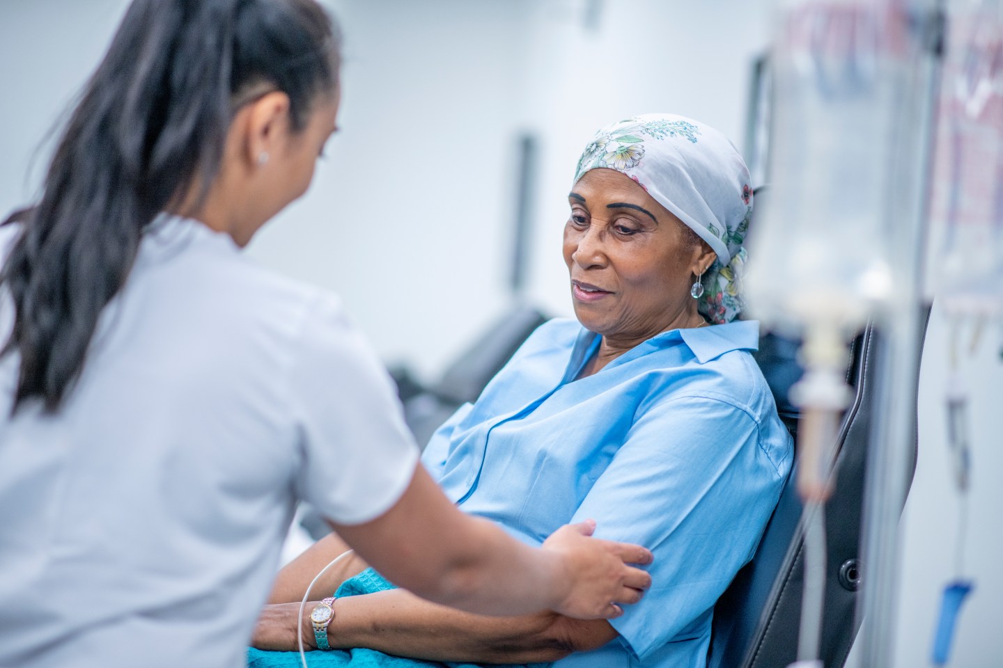 A chemotherapy patient recovers from treatment in a chair as a doctor speaks with her.