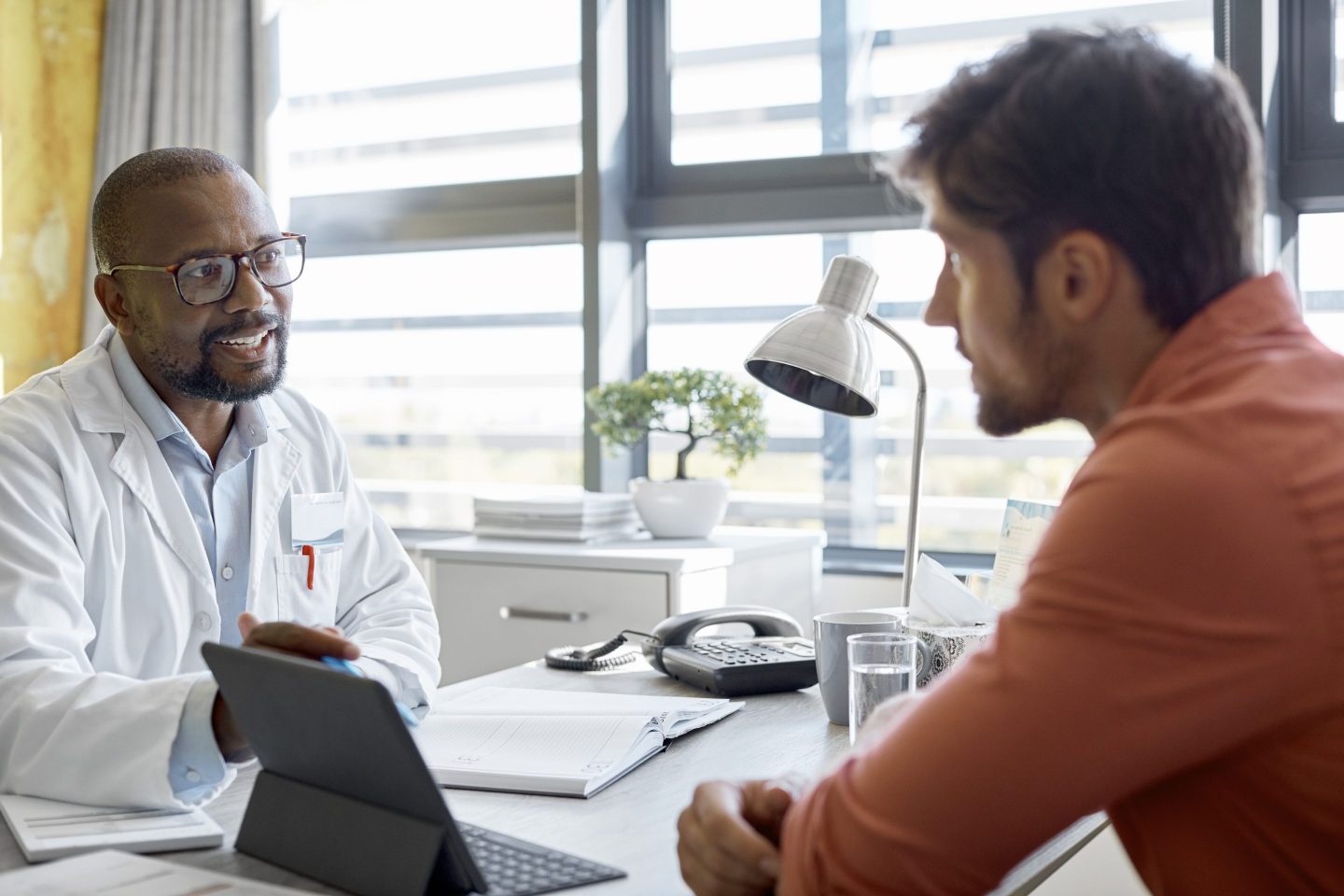 A person in a doctor's coat talking to another person across a table