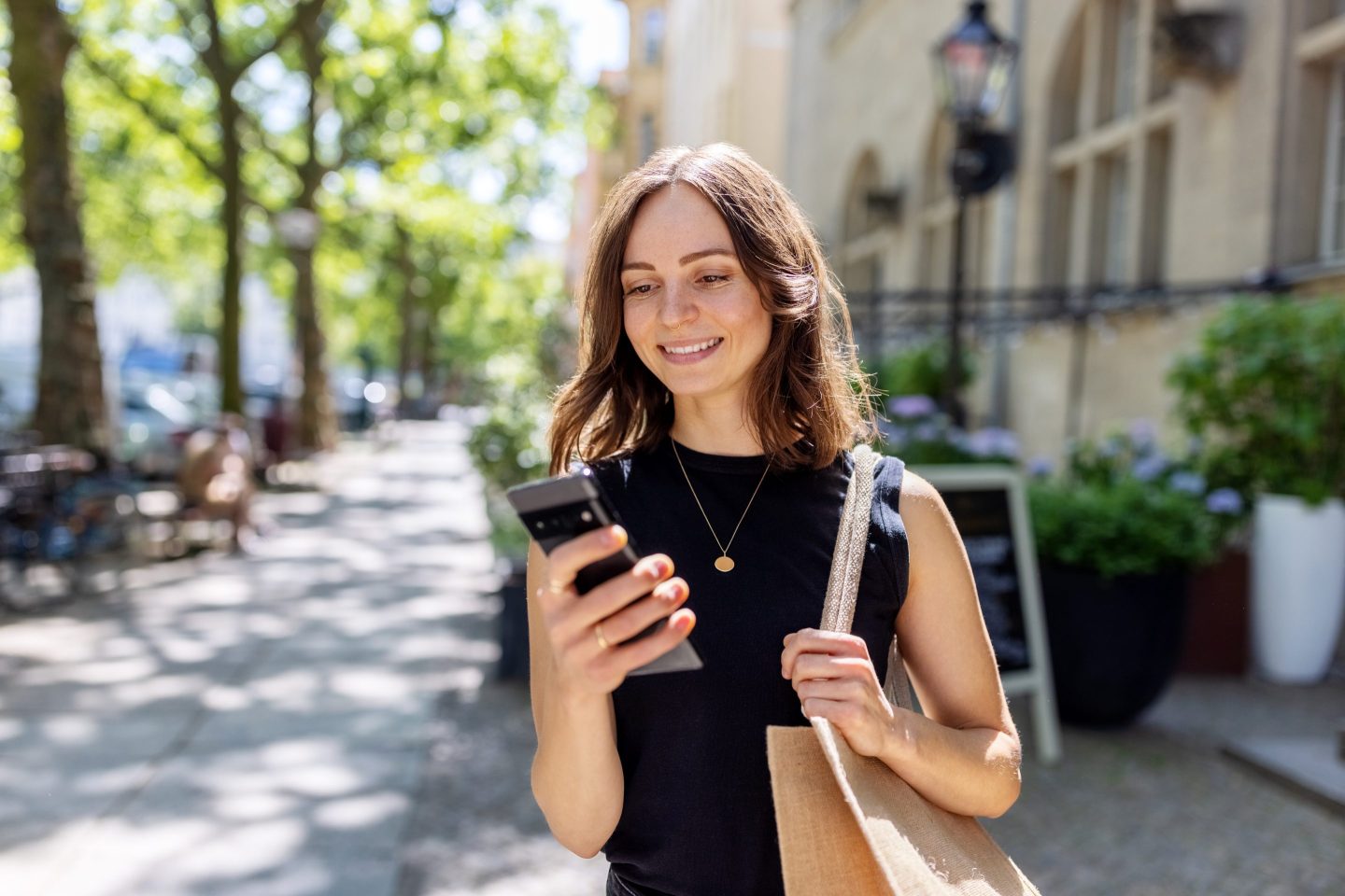 Smiling young woman with smartphone walking on the street