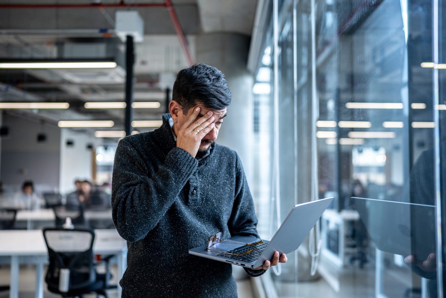 A person standing with his laptop looking stressed