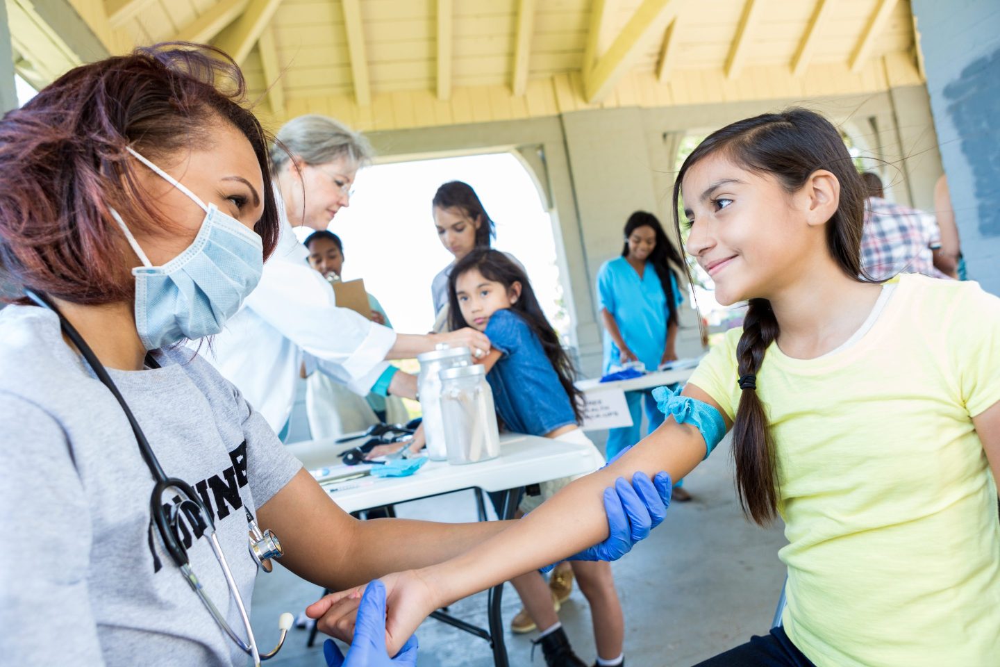 A health care professional prepares to draw blood from a girl's arm