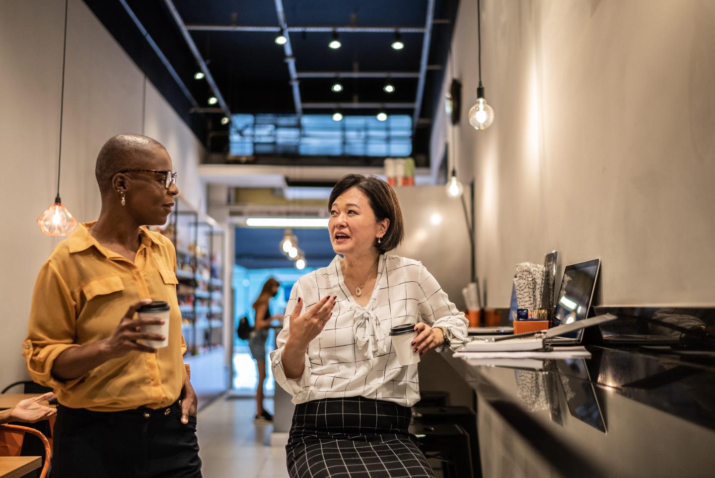 Two businesswomen talk inside a modern coffee shop.