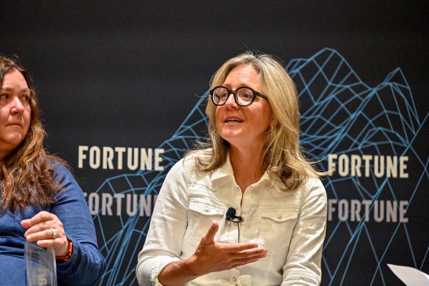 Woman wearing white blouse and glasses speaking on stage