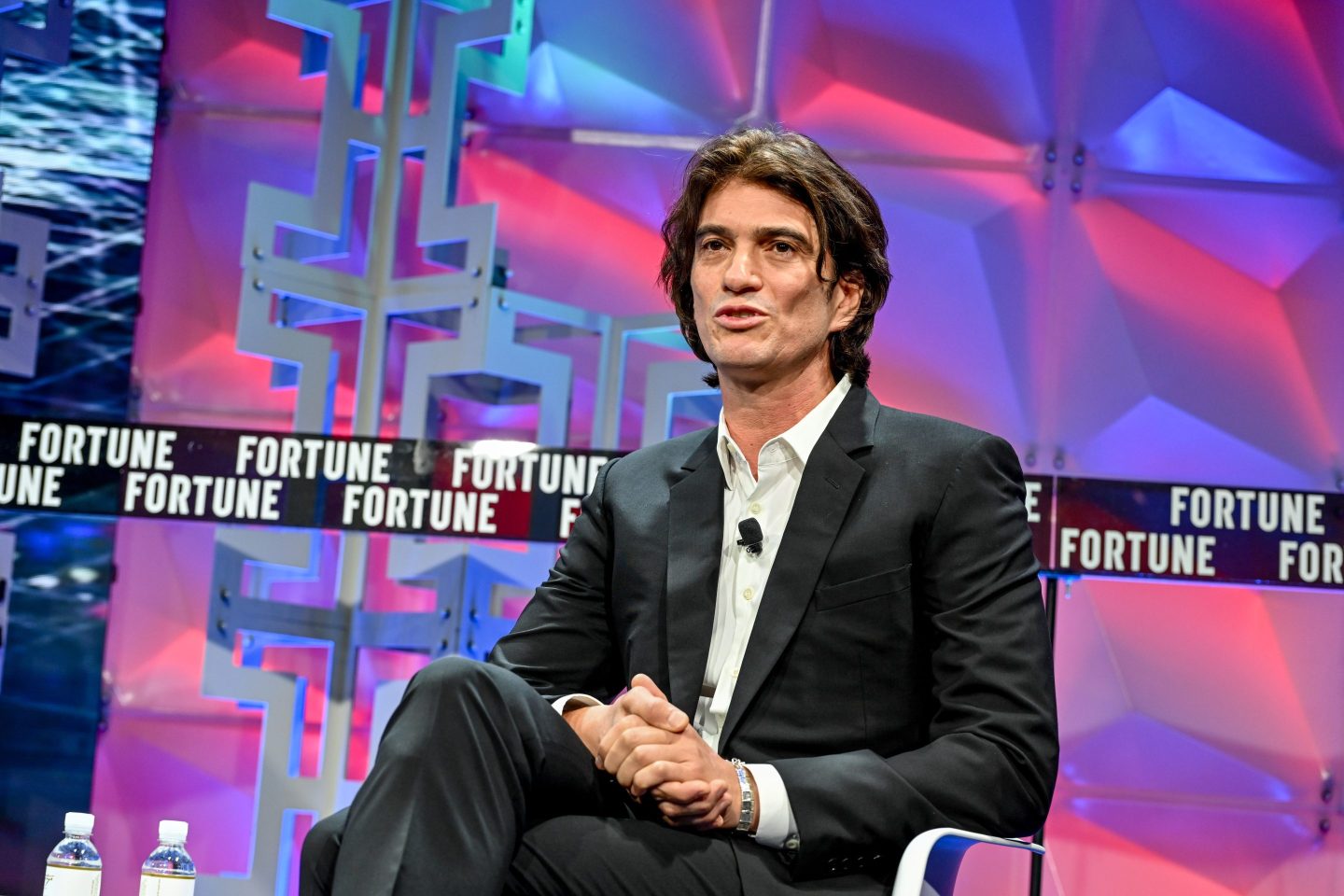 a man in dark suit and collared shirt sits onstage
