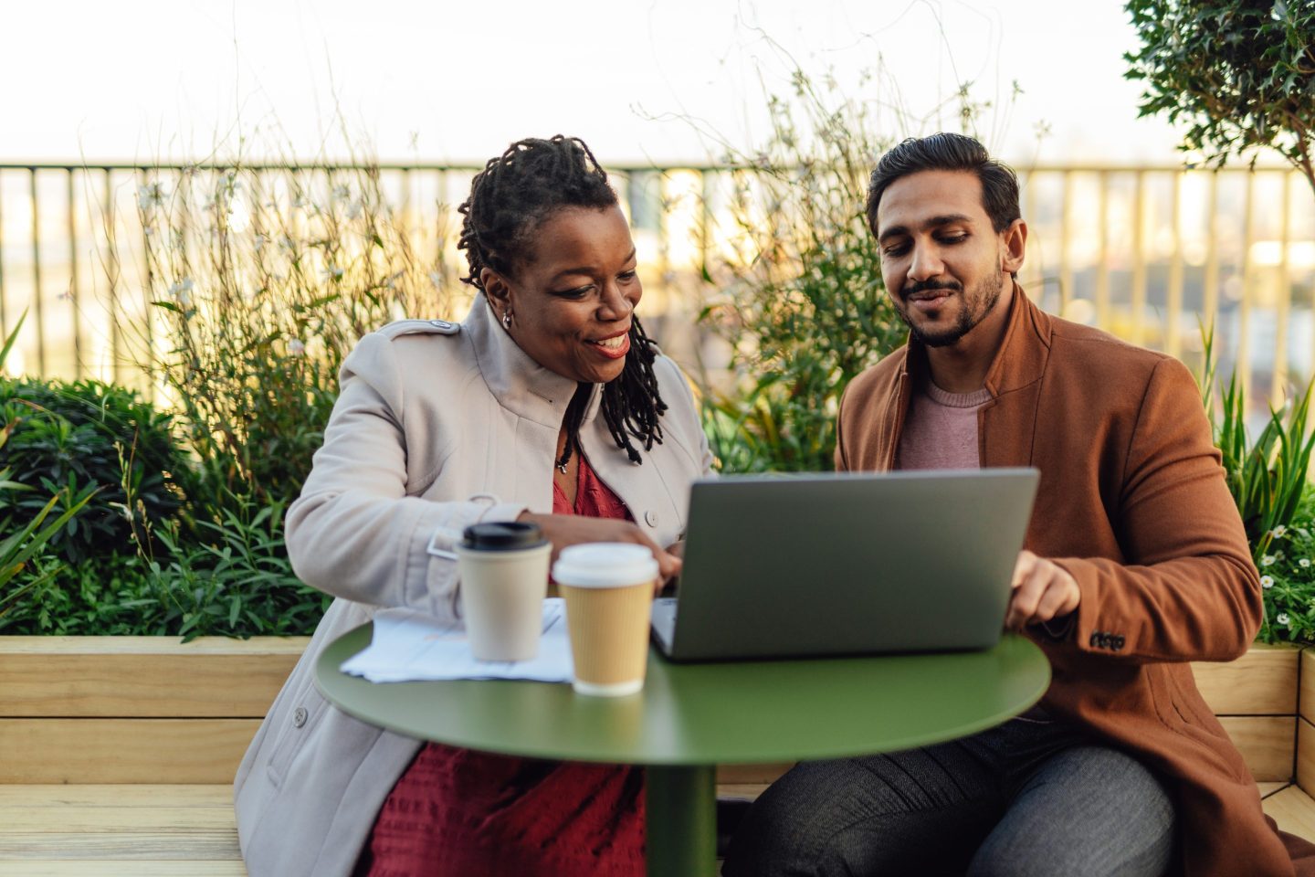 Coworkers discussing project and having work meeting at rooftop garden in high-rise office building