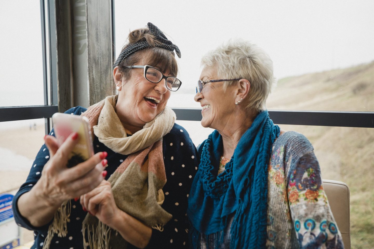 Senior female friends catching up over coffee in a seaside cafe.