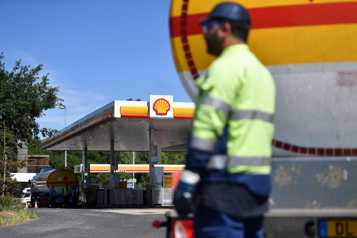 A truck driver stands by the gas container of his truck at a Shell gas station
