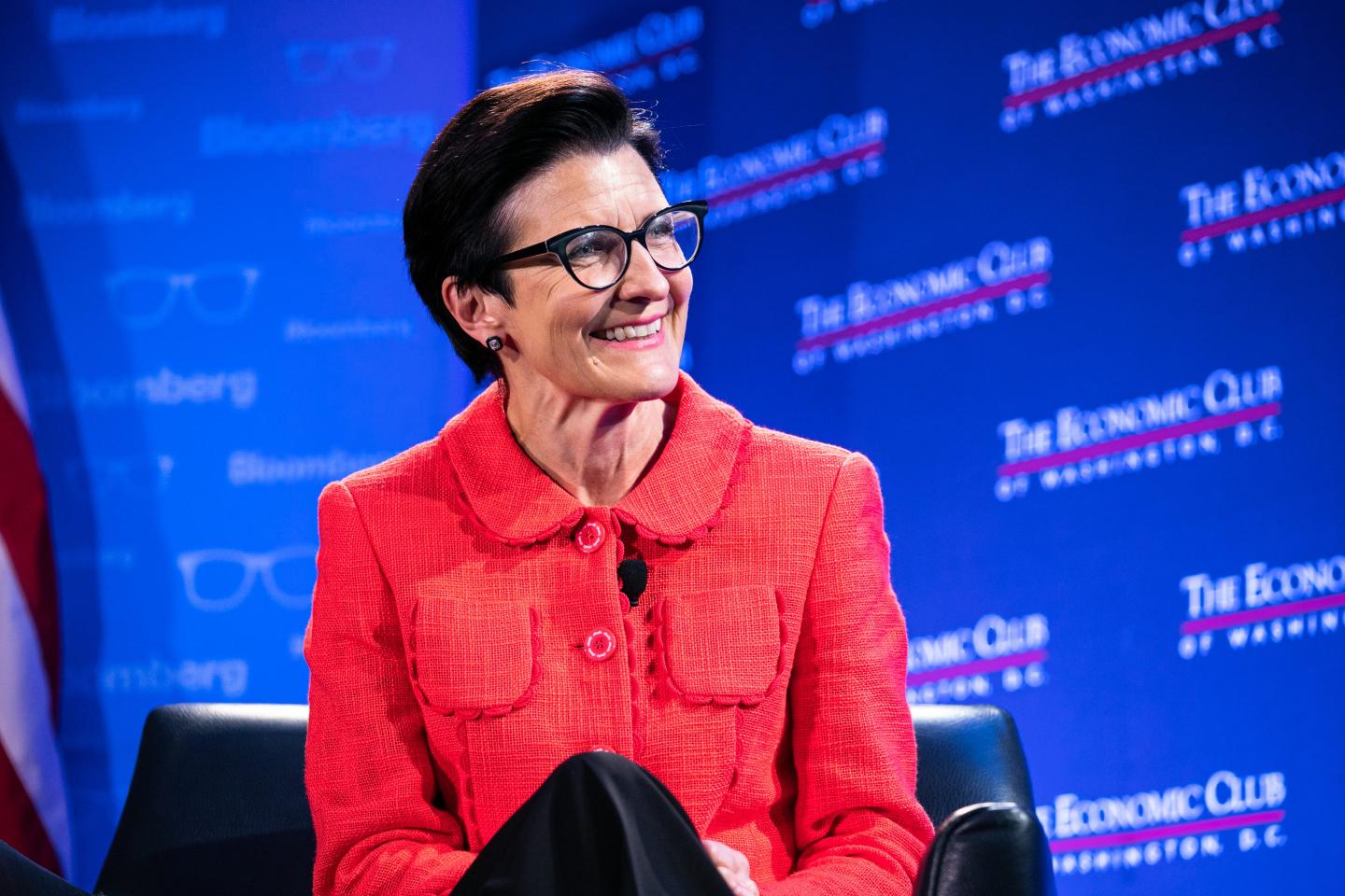 Woman wearing glasses and red jacket sitting on stage