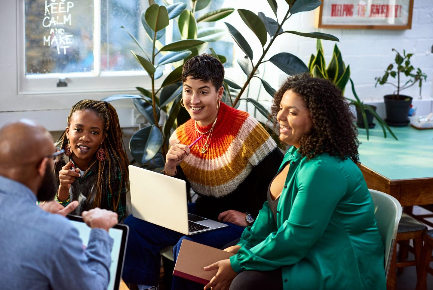 Three business women talk to male colleague in a meeting.