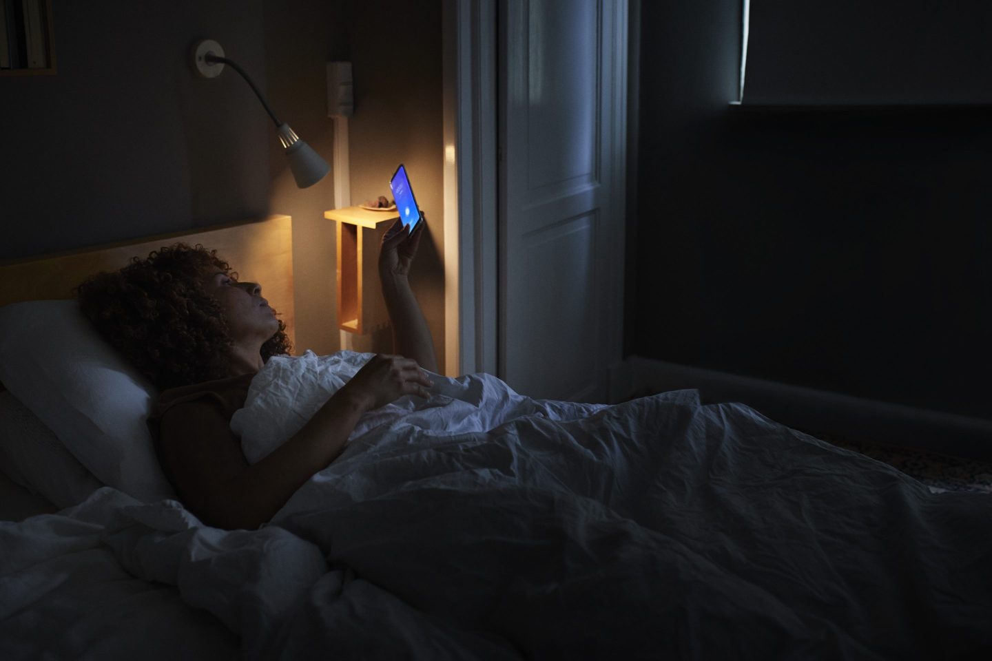 Woman is awake in bed in a darkened room and looking at her phone