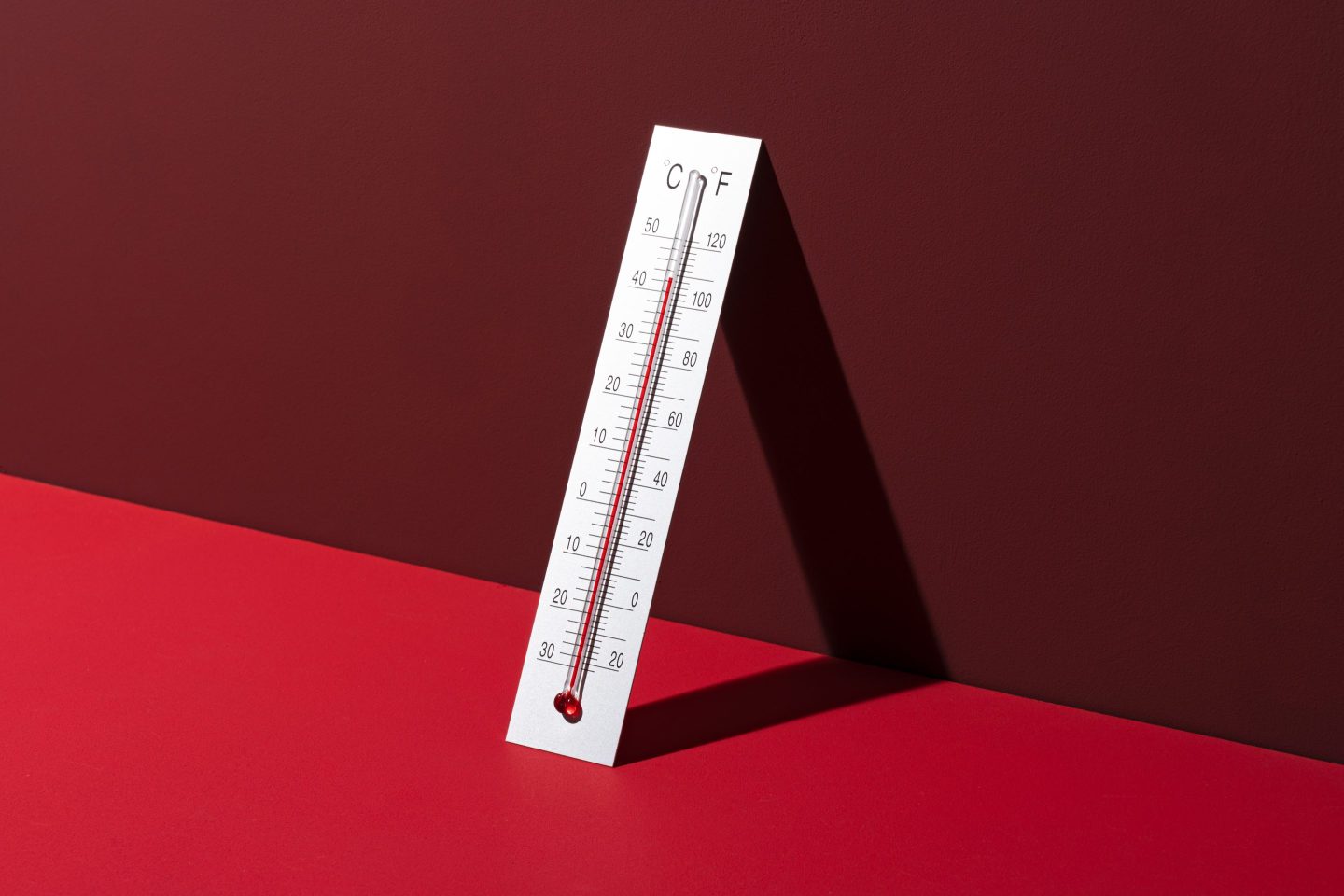 Silver thermometer leaning against red background shows high temperature