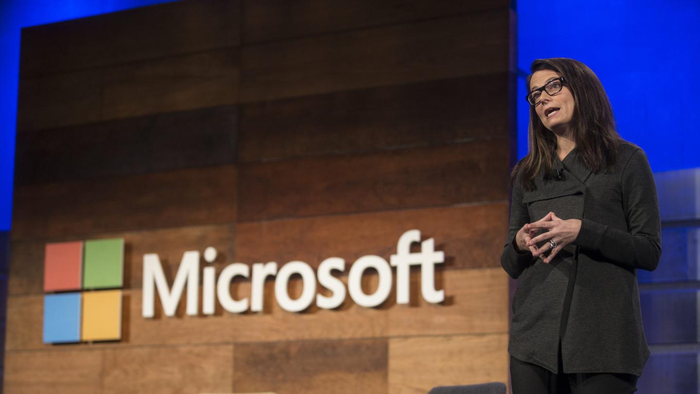 Woman standing and speaking onstage next to the "Microsoft" logo