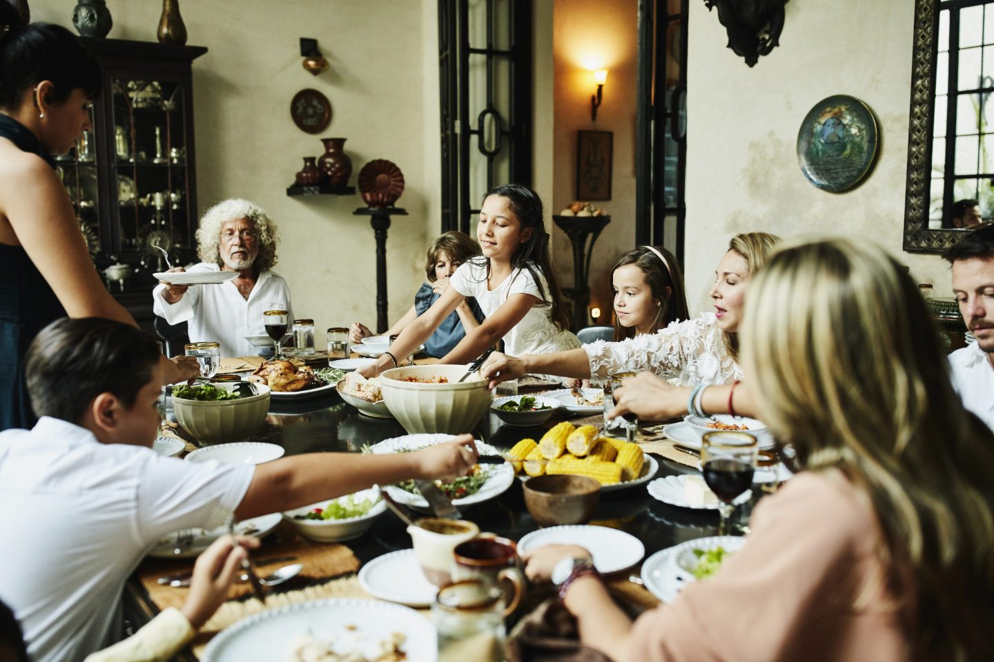 Young girl bringing platter of bread to dining room table during family celebration meal