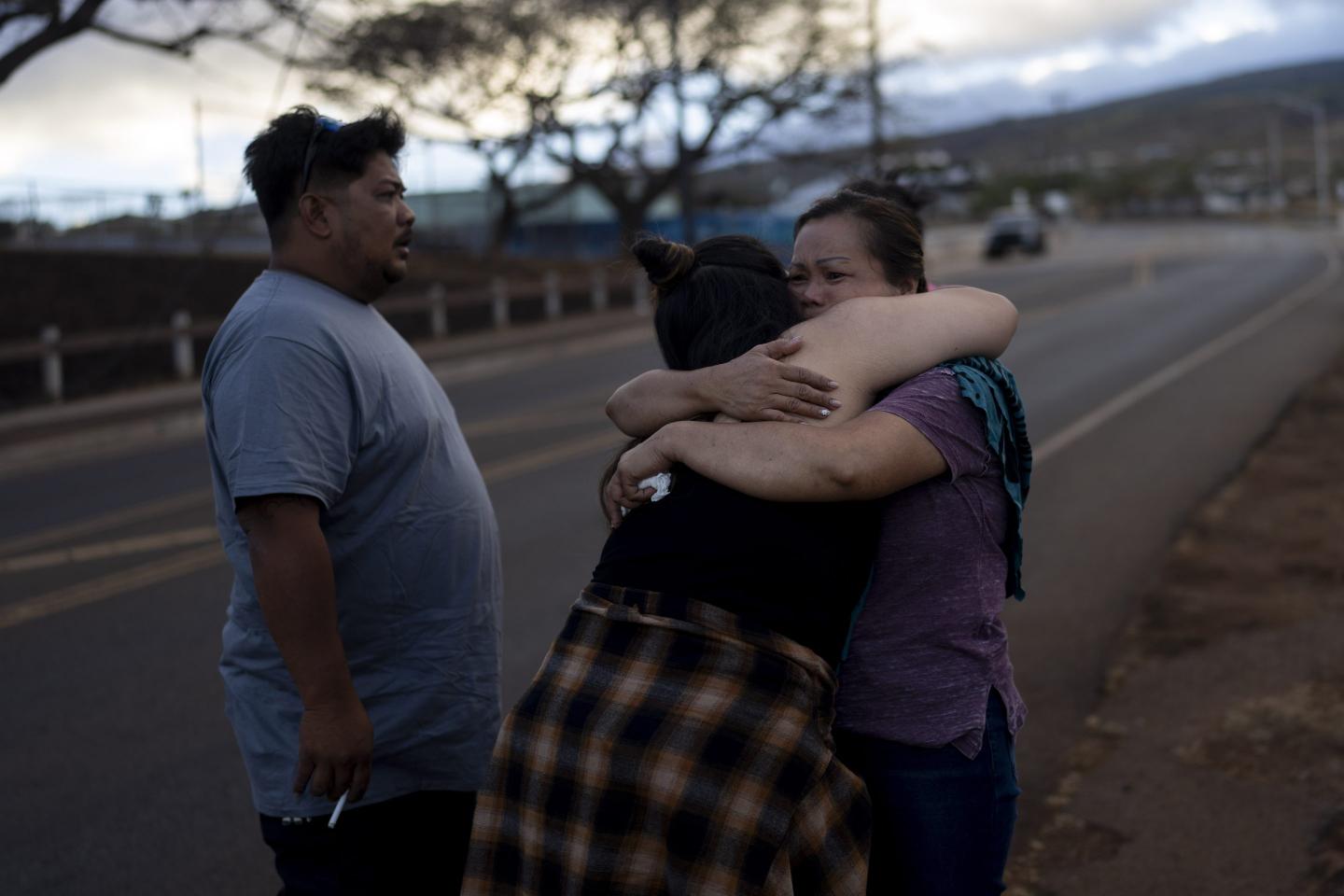 Two women hug and a man looks on with a highway in the background.