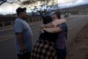 Two women hug and a man looks on with a highway in the background.