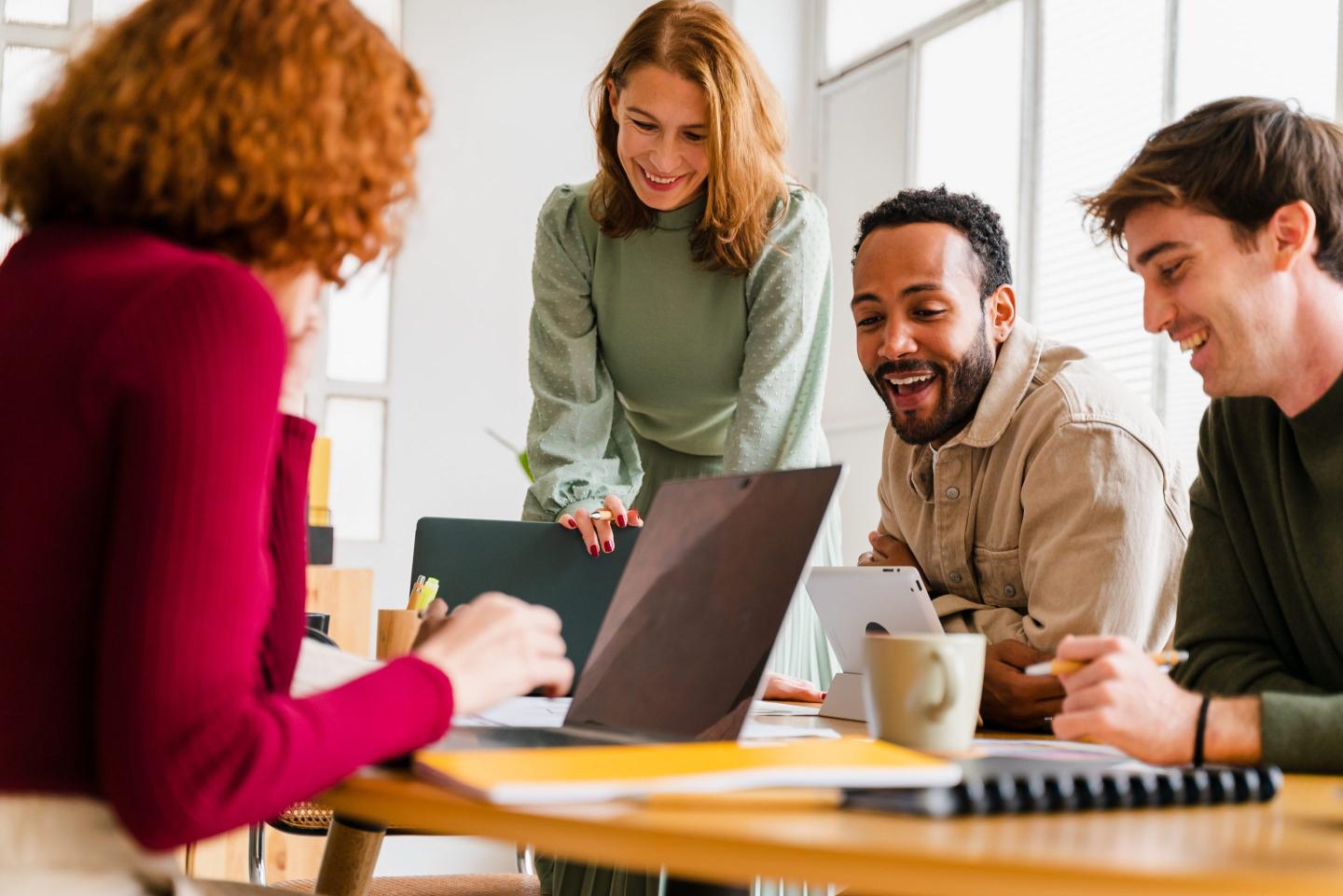 A group of smiling individuals, using laptops and working together on a table