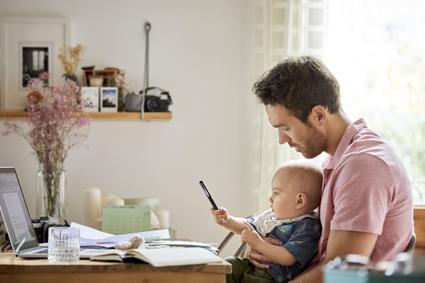 man working at a desk with a baby on his lap