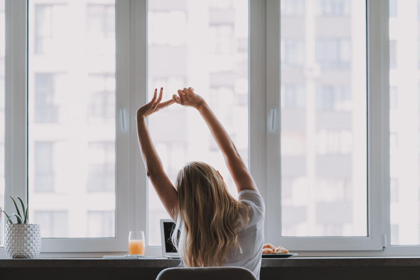 Young woman during a break from work, sitting at a desk and stretching her arms above her head.