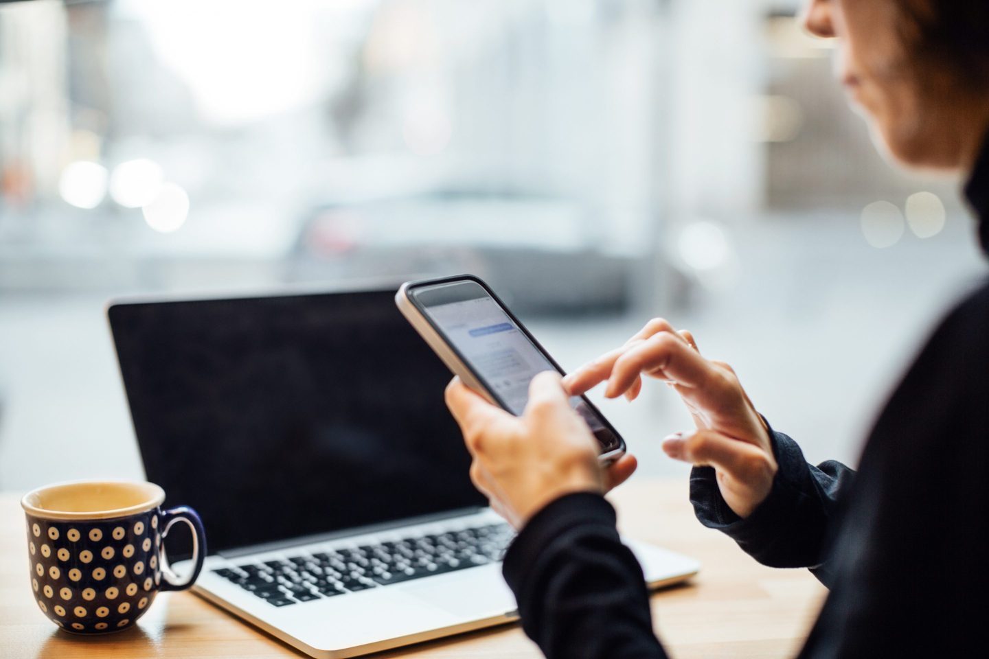 Mature businesswoman sitting at cafe and using cell phone with a laptop on table. Mid adult female texting with her smart phone at coffee shop.