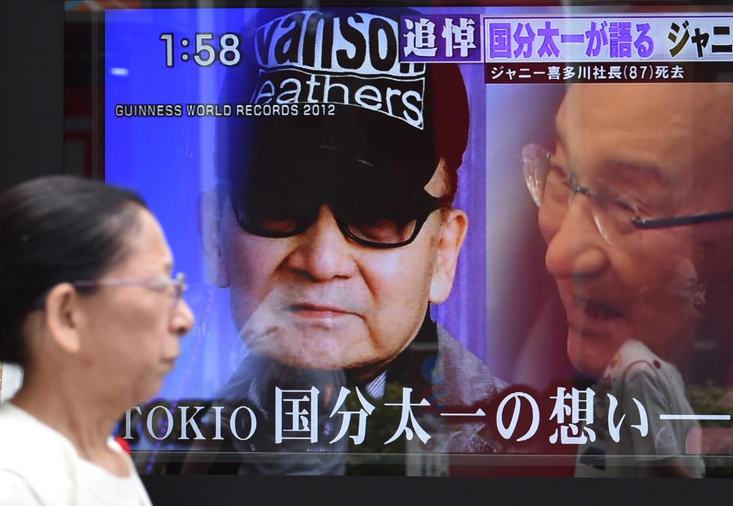 A woman walks past a roadside television screen reporting the death of Johnny Kitagawa, founder of Japanese talent agency Johnny & Associates