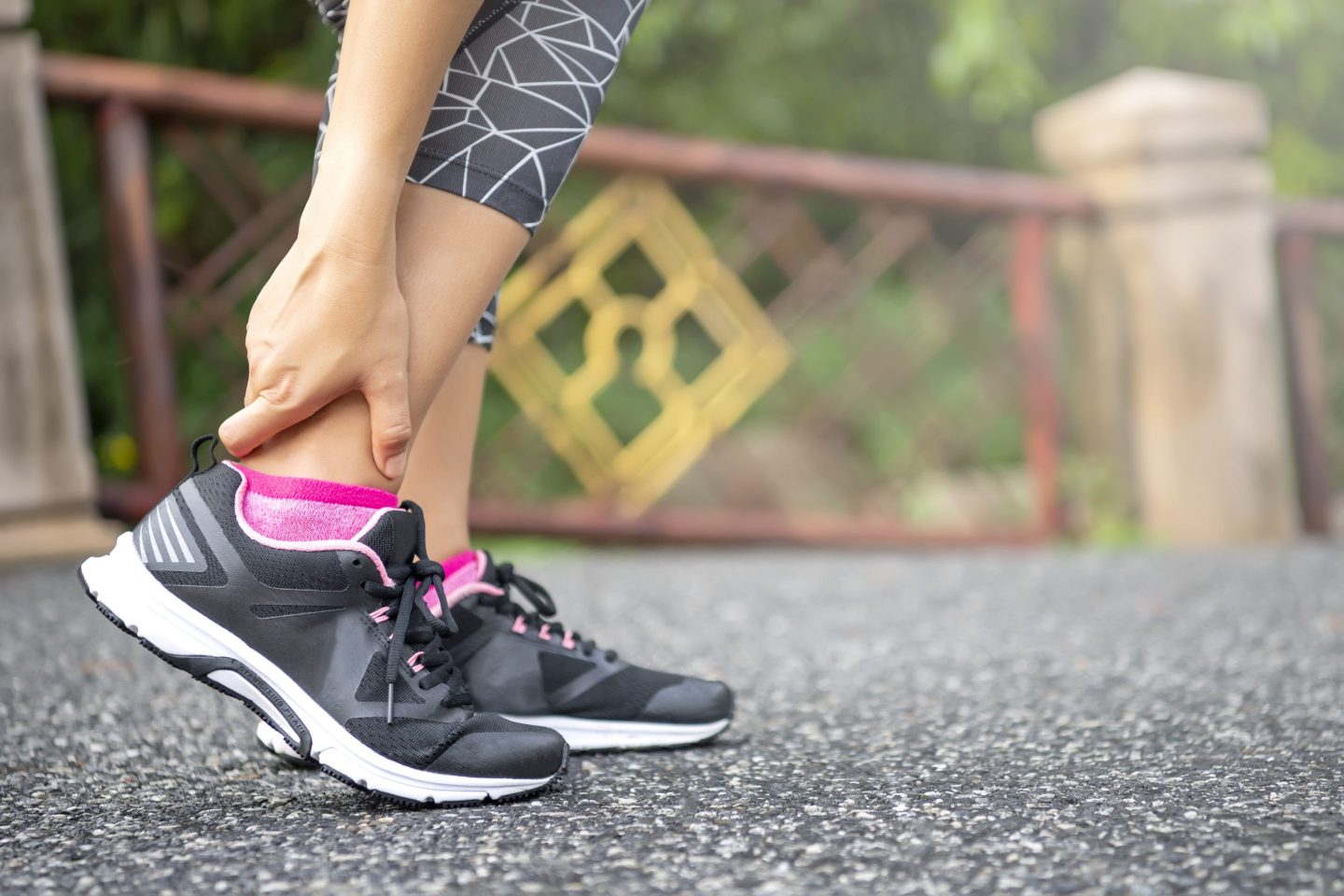 Close-up of woman standing on road and holding her injured ankle after jogging.