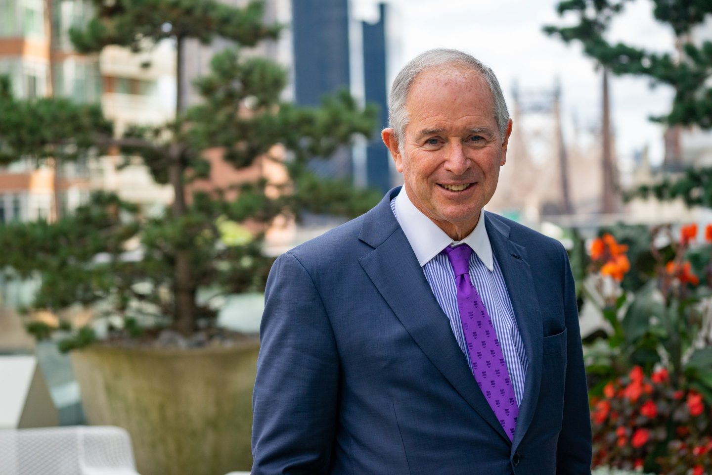 man in suit and purple tie posing in front of potted plants