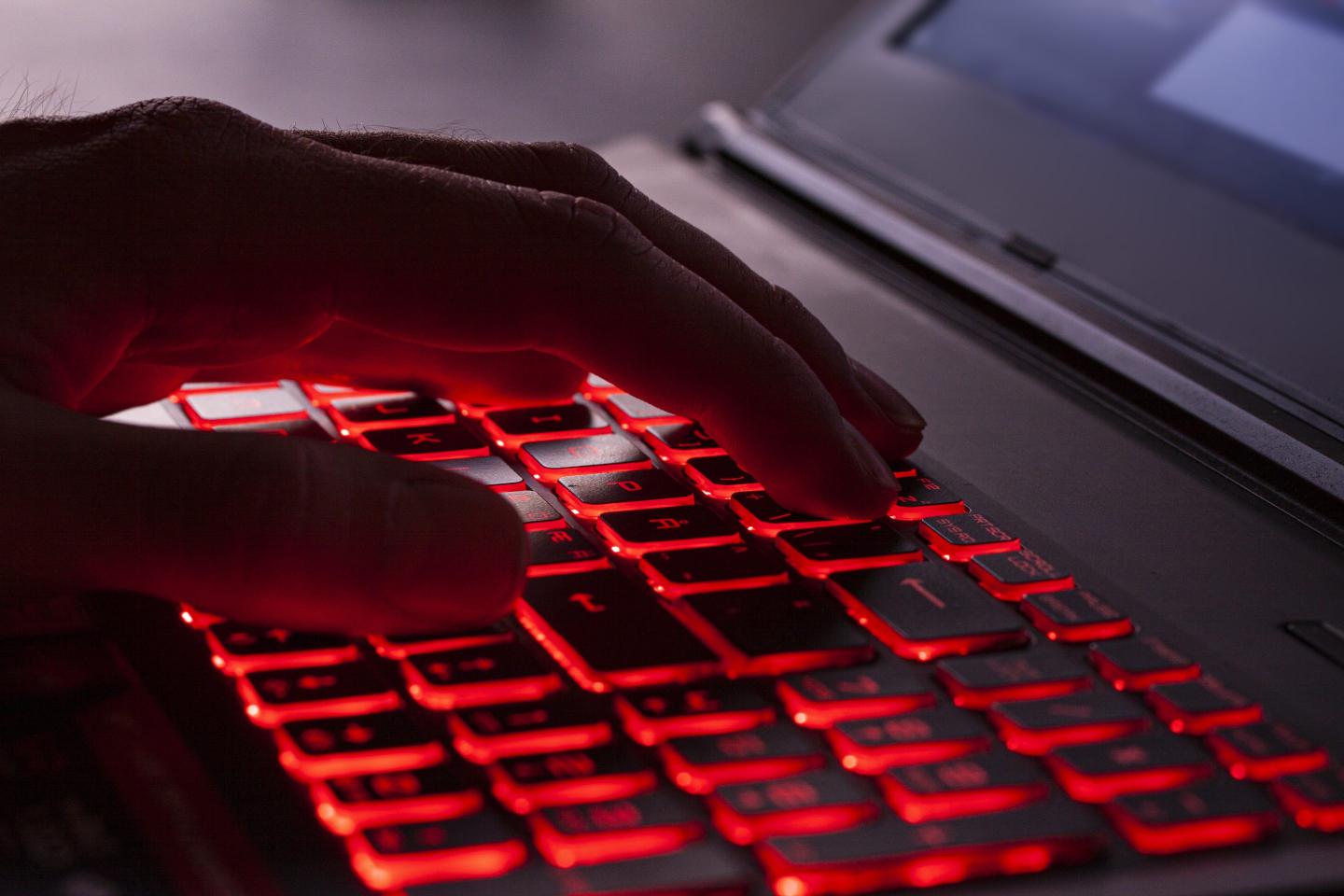Close up of fingers typing on glowing red backlight keys on a computer keyboard.